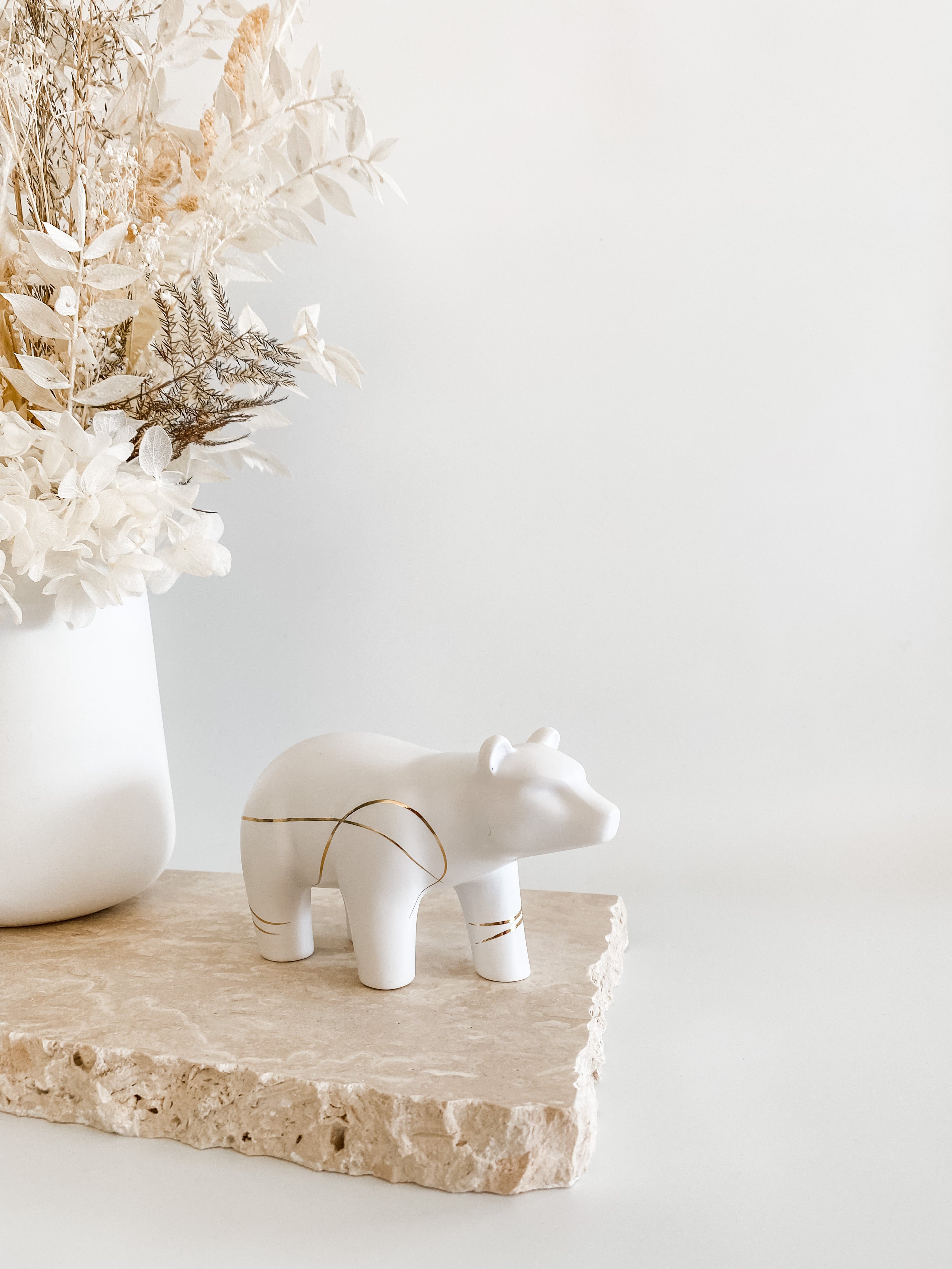 a white vase with flowers and a white bear figurine